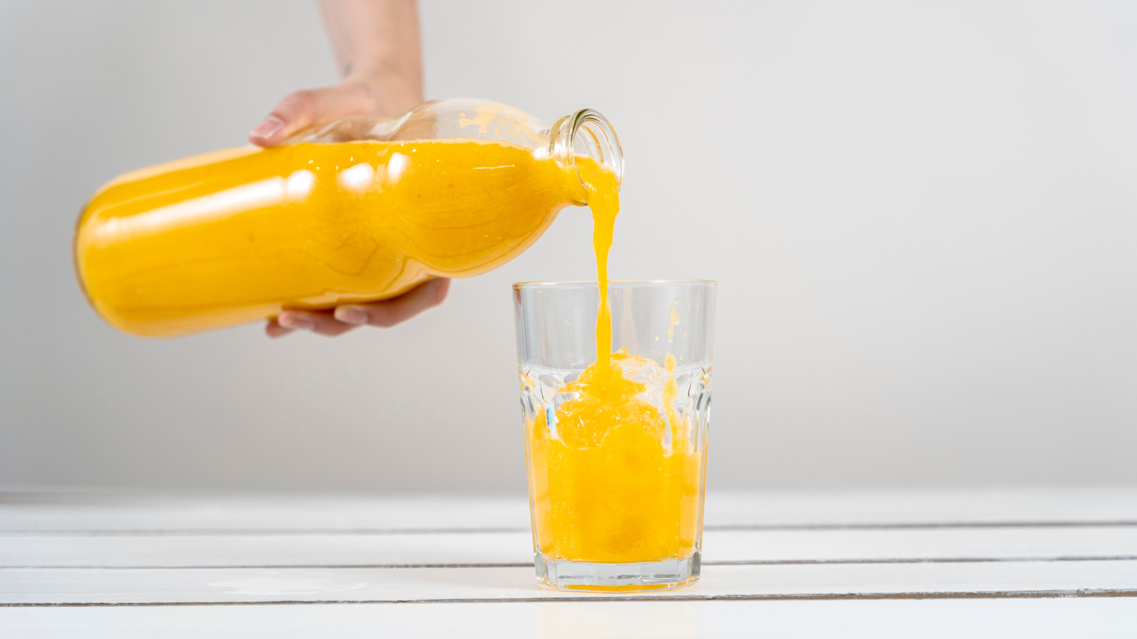 Alguém enchendo um copo com suco de laranja